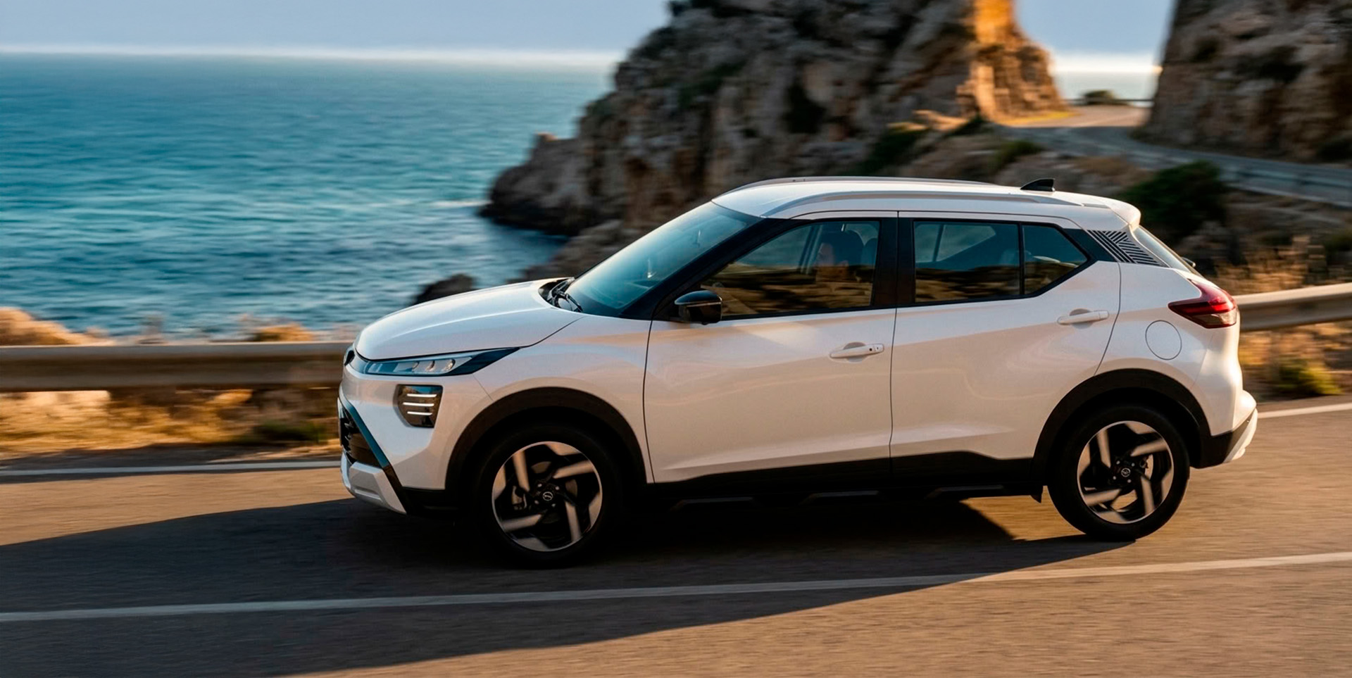 Nissan Kait branco estacionado à beira-mar, com rochas ao fundo