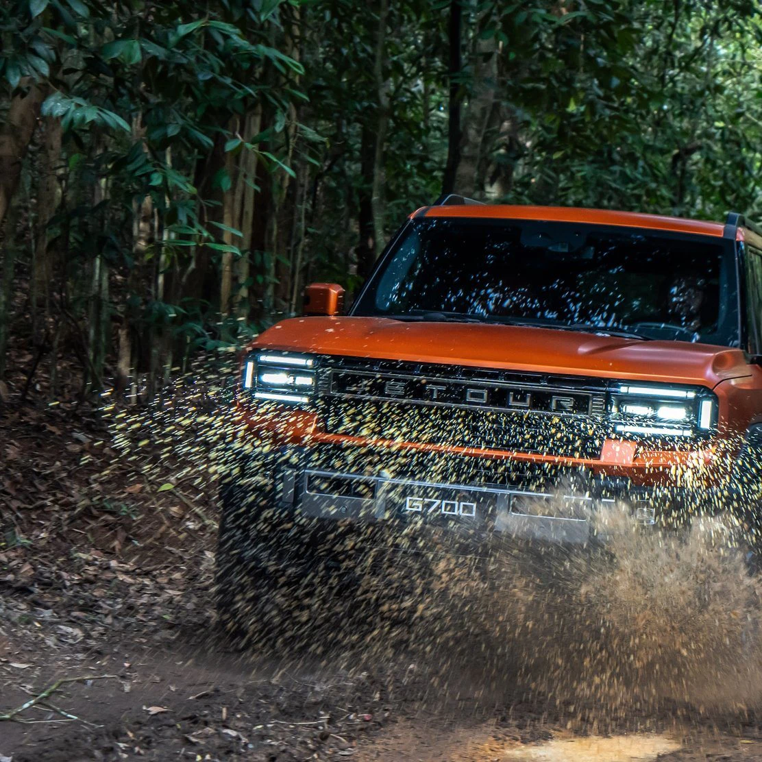 JETOUR G700 laranja atravessando uma poça de lama numa trilha na mata