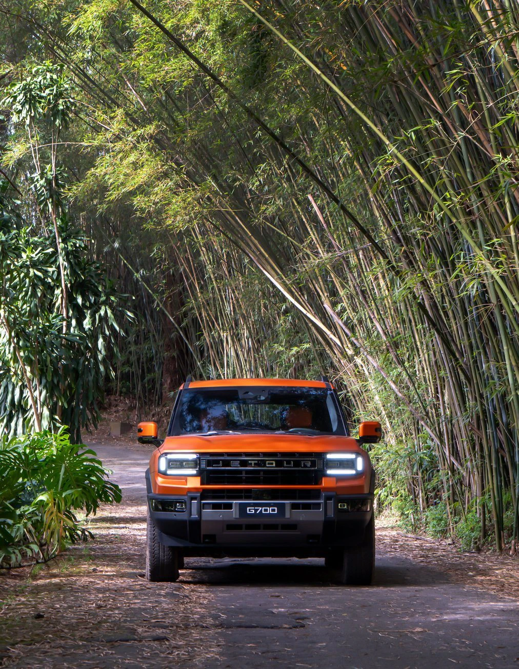 JETOUR G700 laranja de frente numa estrada de terra cercada por bambus